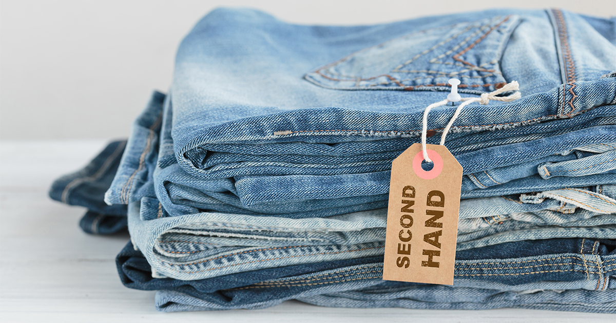 Stack of folded second-hand denim jeans with a brown recycled paper tag labeled “Second Hand”.