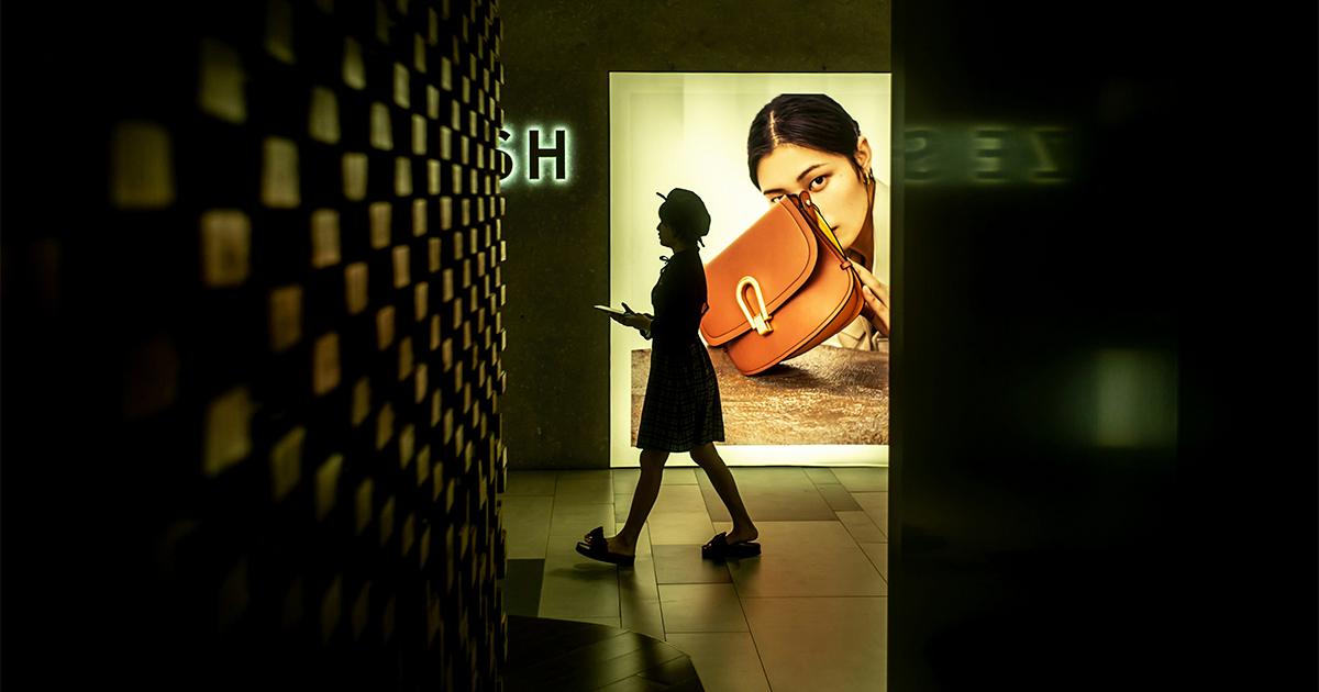 Silhouette of a shopper walking past a luxury retail store display featuring a high-end advertisement