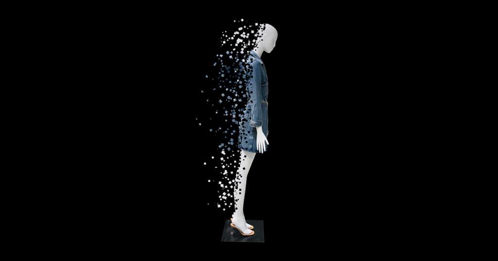 Side view of a mannequin wearing a denim dress, gradually dissolving into scattered digital pixels against a black background.