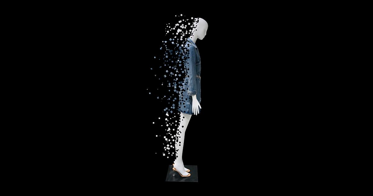 Side view of a mannequin wearing a denim dress, gradually dissolving into scattered digital pixels against a black background.