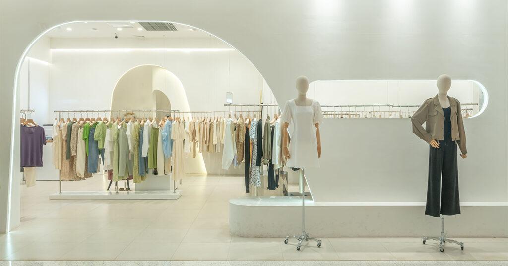 White minimalist store interior with mannequins in women’s outfits and racks of clothing.