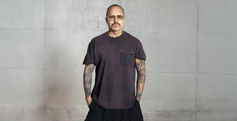 Portrait of designer Willy Chavarria in front of a grey slab background.
