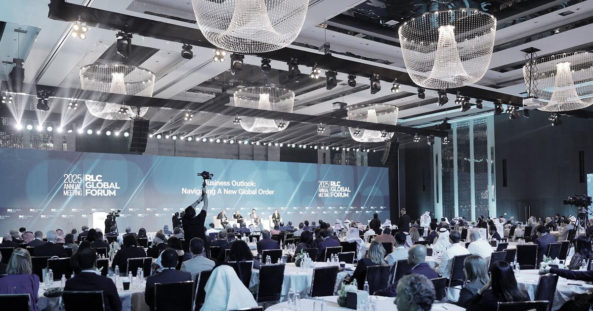 A large conference ballroom filled with attendees facing a stage with a panel of speakers. at the RLC 2025 Annual Forum. Bright stage lighting and multiple crystal chandeliers hang from the ceiling.