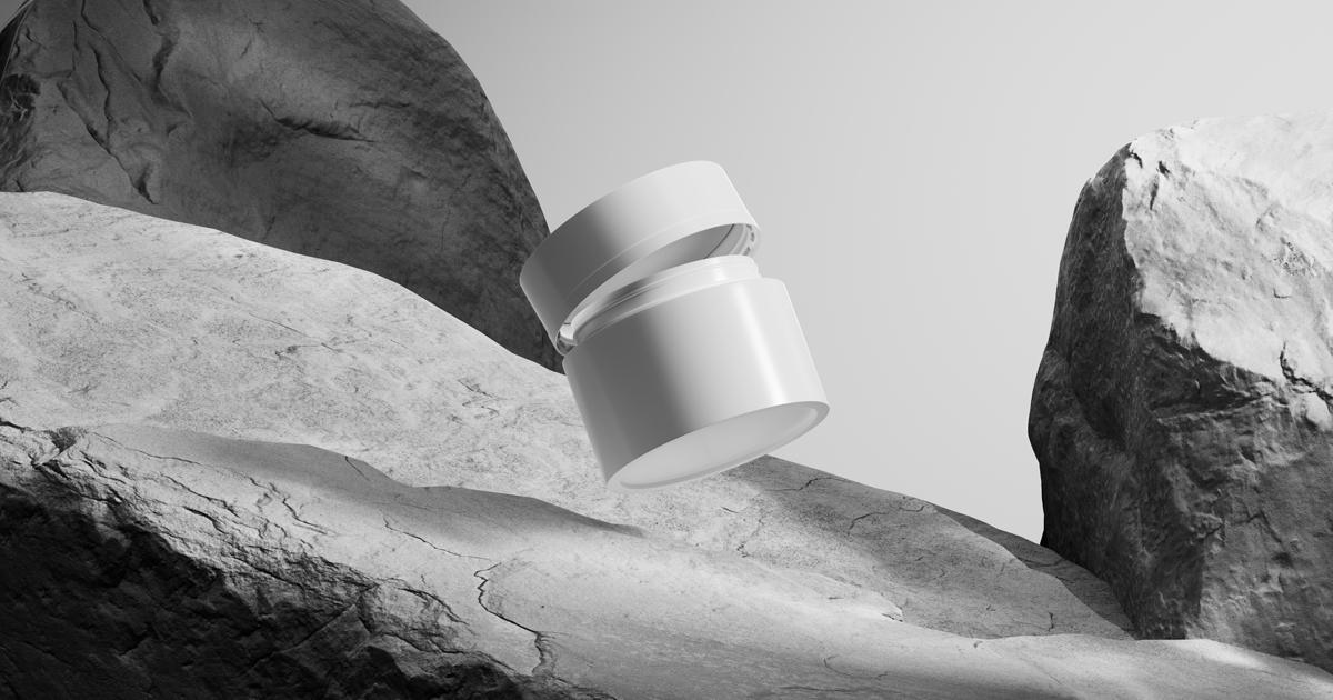 Black and white image of an open white cosmetic jar floating among a desert-like setting of large stone rocks.