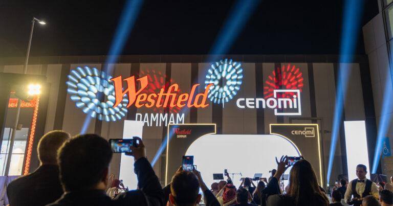 Crowd attending the launch of Westfield Dammam, with the Westfield and Cenomi Centers logos illuminated on the mall’s exterior and lights projecting into the night sky.