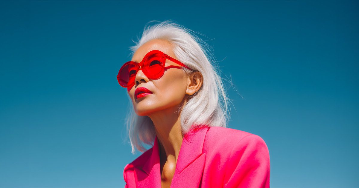 Portrait of a mature Asian woman with white hair, wearing bold red sunglasses and a fuchsia blazer.