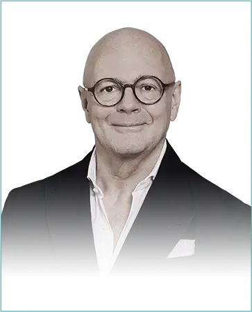 Portrait of André Maeder, CEO of Selfridges Group, wearing glasses and a suit against a teal background.