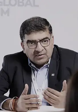 Middle-aged man with dark hair and glasses, wearing a blazer and lanyard, speaking and gesturing with his hands during a panel discussion.