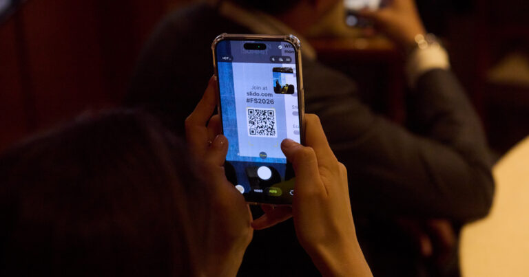 Audience member holding up a smartphone to scan a Slido QR code during the 2026 RLC Fashion Summit in Milan.