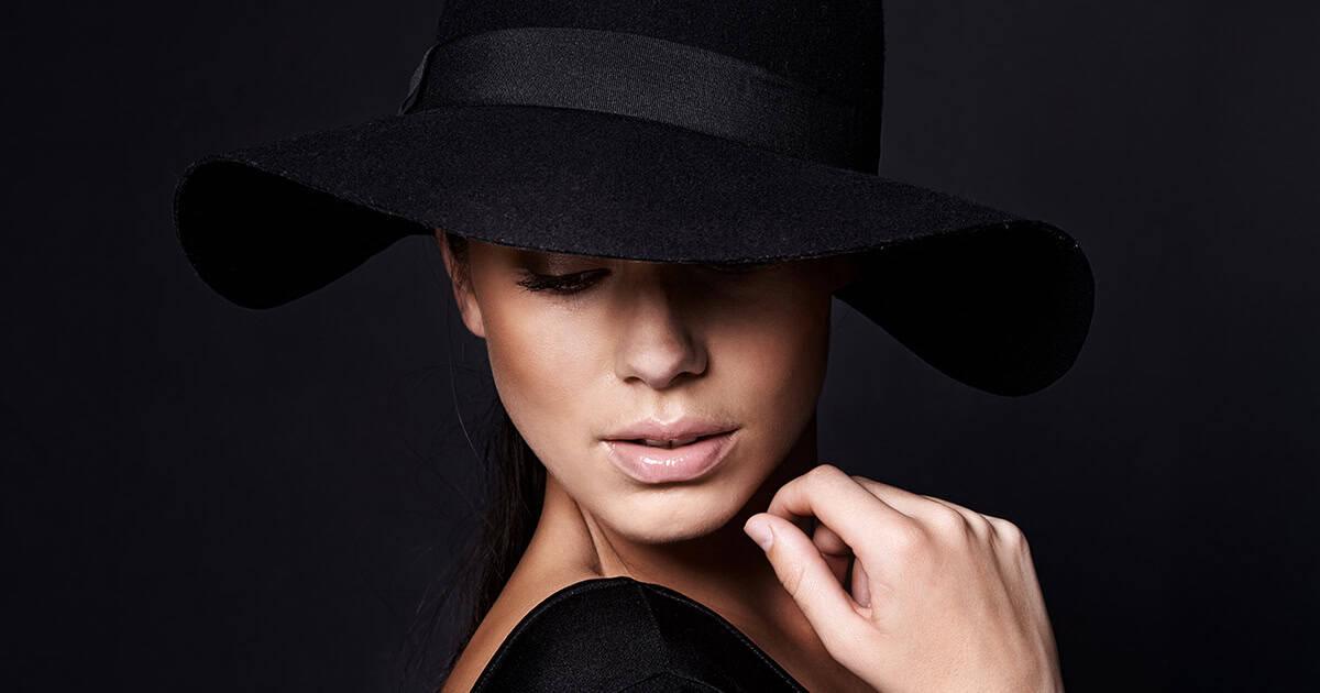 Woman wearing a black wide-brim hat looking downward against a dark background at RLC Global Forum.