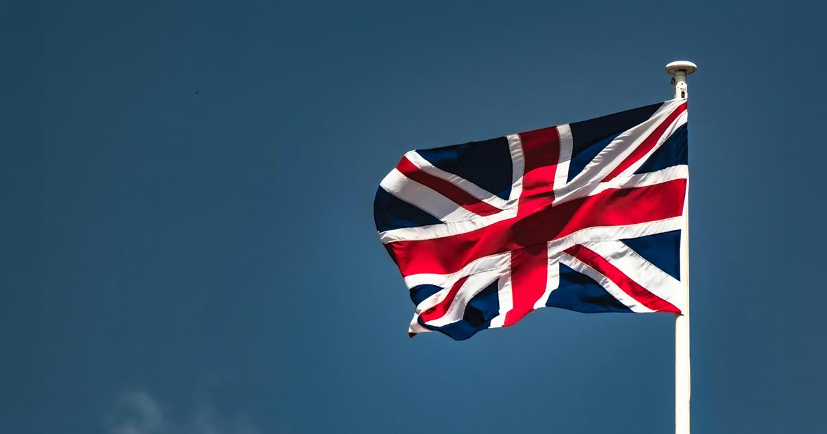 A Union Jack flag flying in the wind against a clear blue sky.