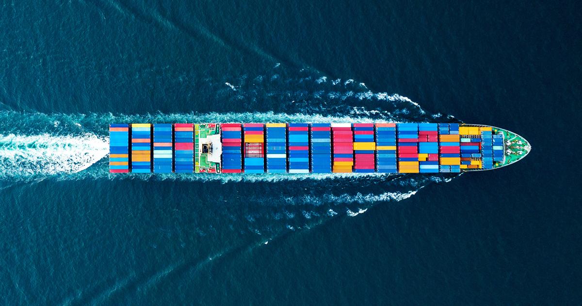 Aerial view of a large container ship carrying cargo across deep blue water.