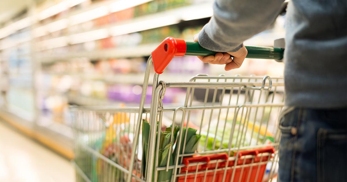 Close-up of a shopper pushing a grocery cart filled with fresh produce down a supermarket aisle, highlighting evolving behavior, value-driven purchasing and new trends in grocery retail.