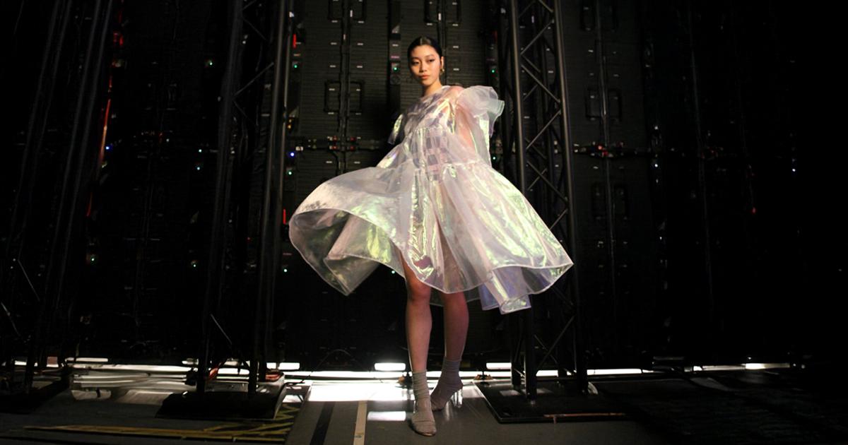 Young model in a shimmering dress stands backstage under stage lighting, evoking questions about material waste, innovation, and the environmental cost of fashion.