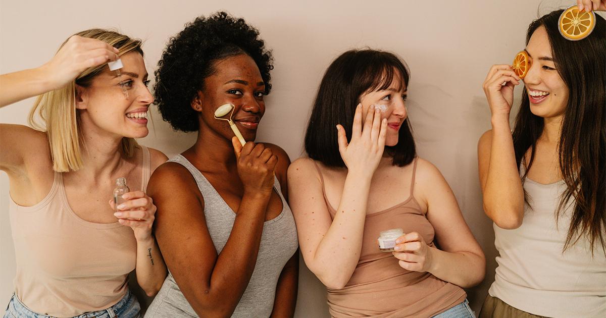 Diverse group of four women using various skincare tools and products together against a beige background at RLC Global Forum.