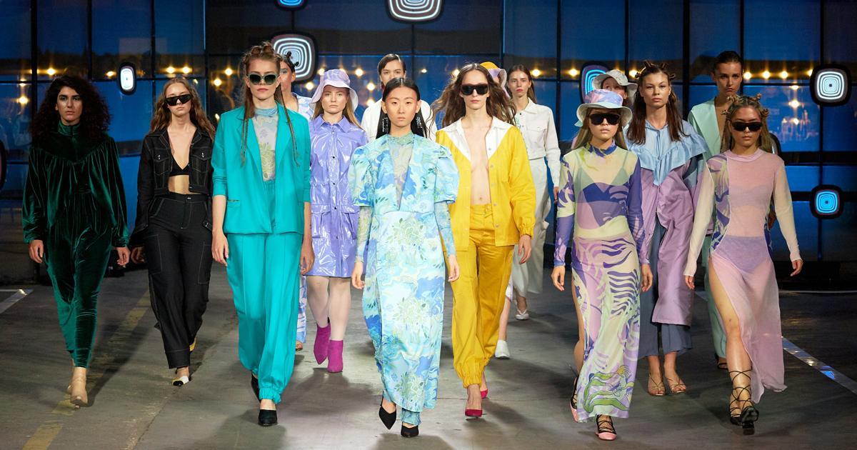 Models walking down a runway in colorful looks during a fashion show.
