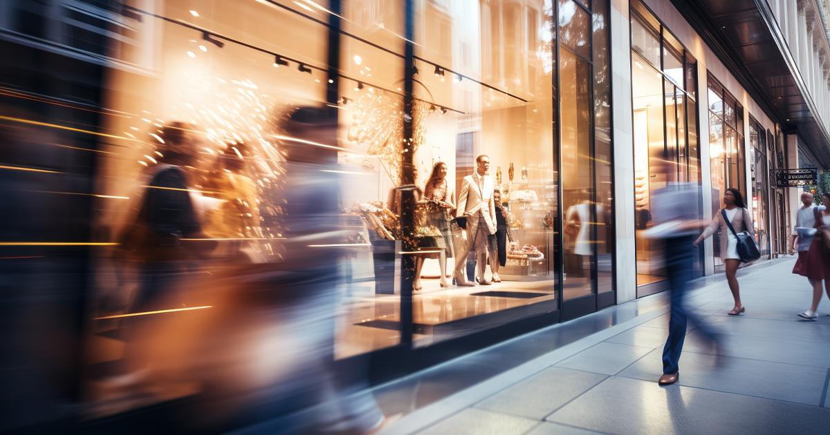 Blurred silhouettes of shoppers passing store windows on a UK high street.