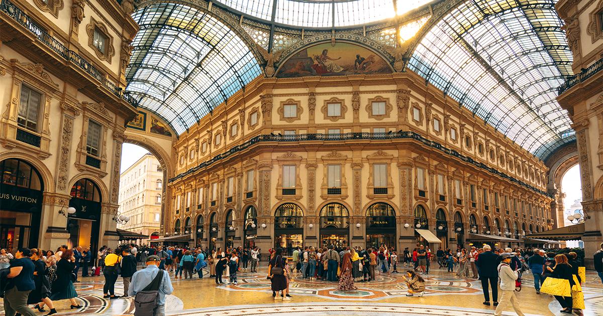 A crowded indoor shopping arcade with classical architecture and a vaulted glass dome roof at RLC Global Forum.