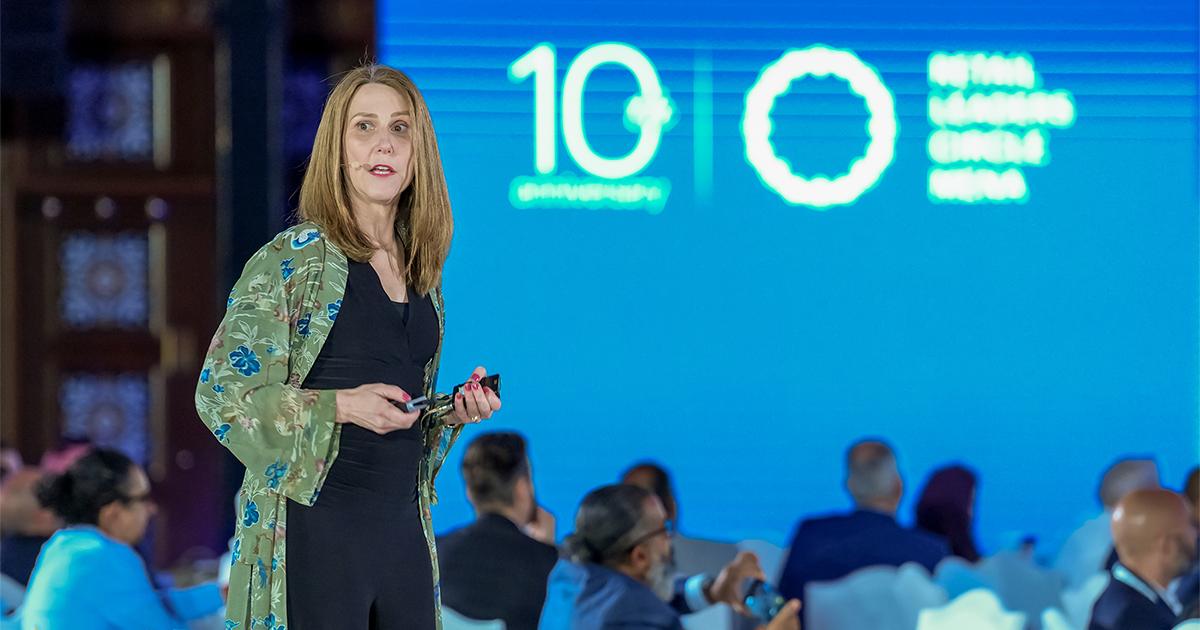 A female keynote speaker delivering a presentation on stage in front of a blue background at RLC Global Forum.
