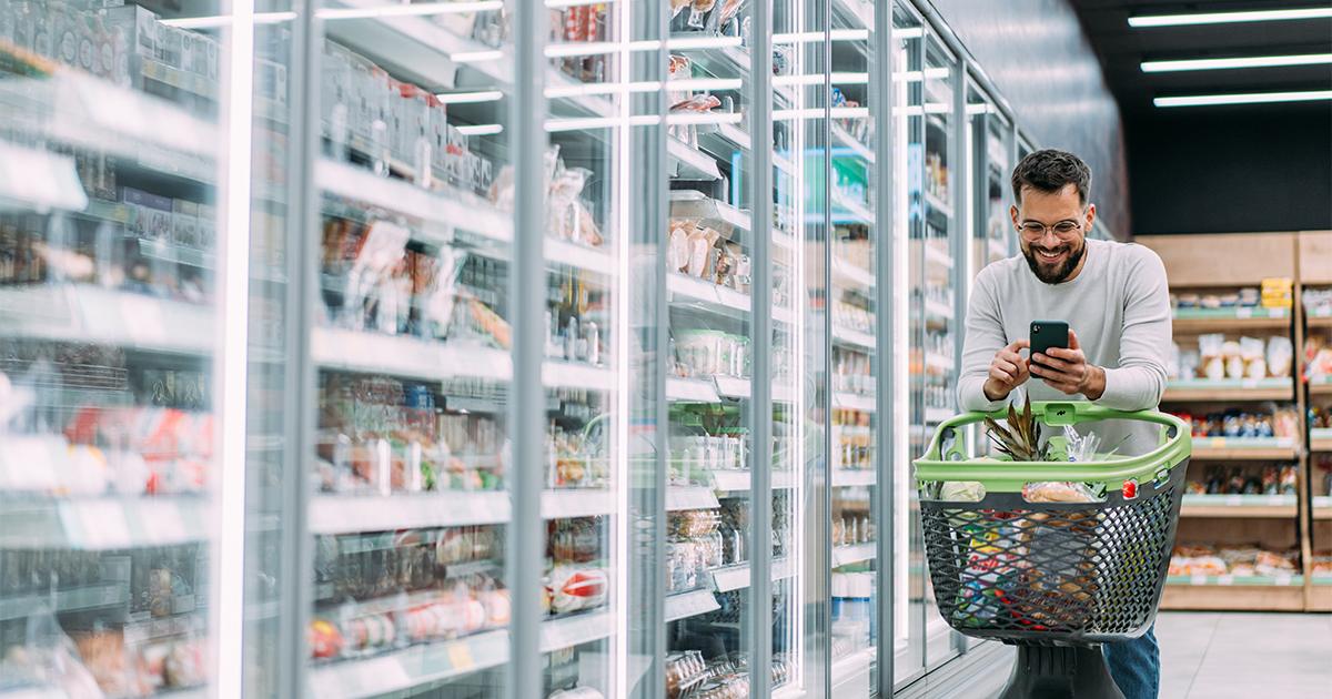 Man grocery shopping in supermarket with smartphone