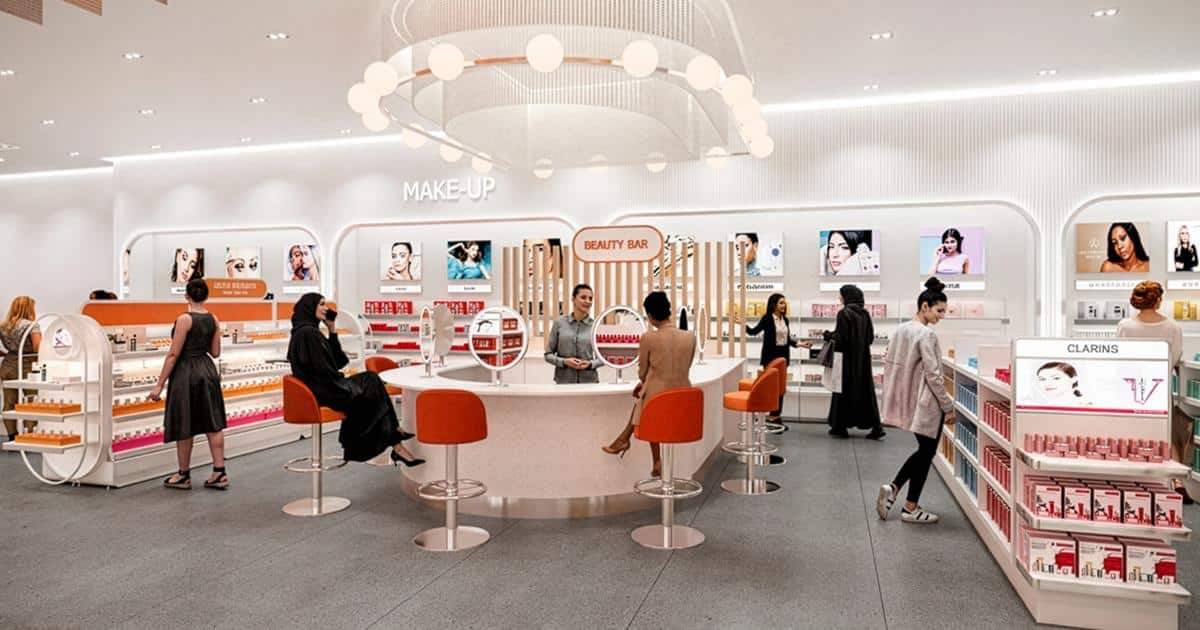 Interior of an Ulta Beauty store, featuring makeup displays, a central Beauty Bar with orange stools, and customers browsing products under bright lighting.