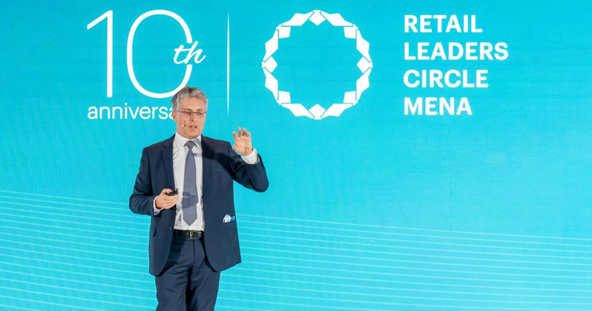 A male corporate executive presenting on stage in front of a blue background with Retail Leaders Circle MENA branding at RLC Global Forum.
