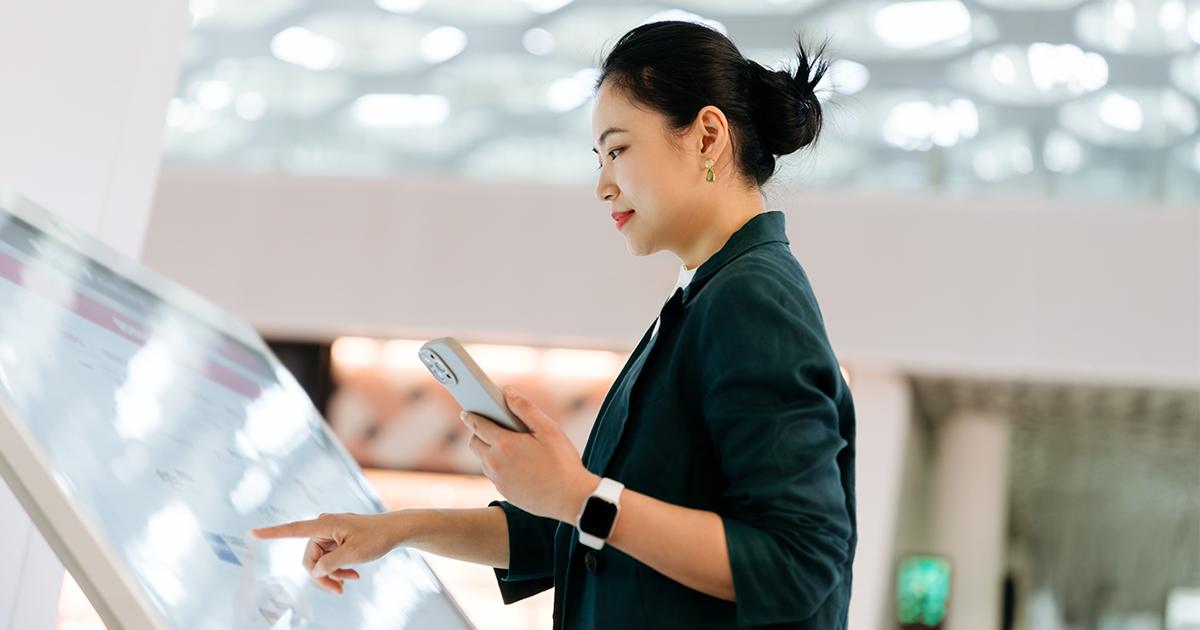A woman using a smartphone while interacting with an interactive digital display screen at RLC Global Forum.