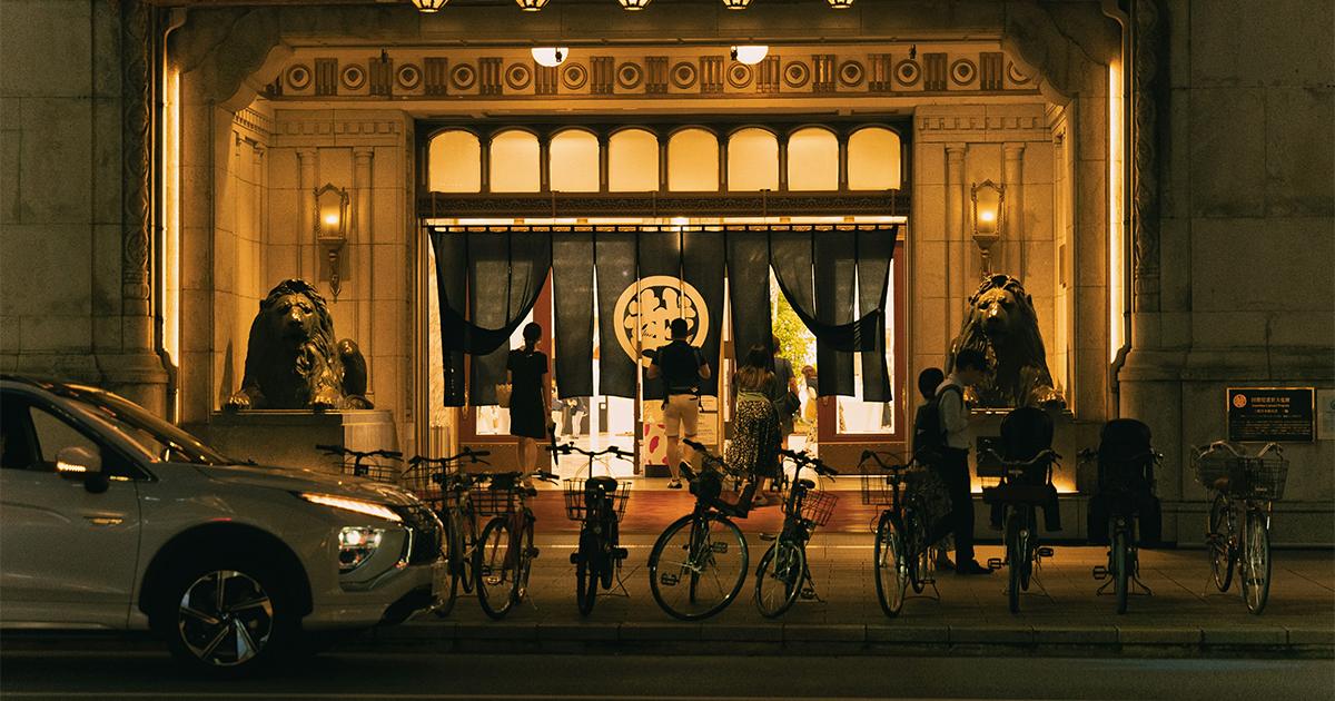 People enter a department store with lion statues at the entrance, illuminated at night