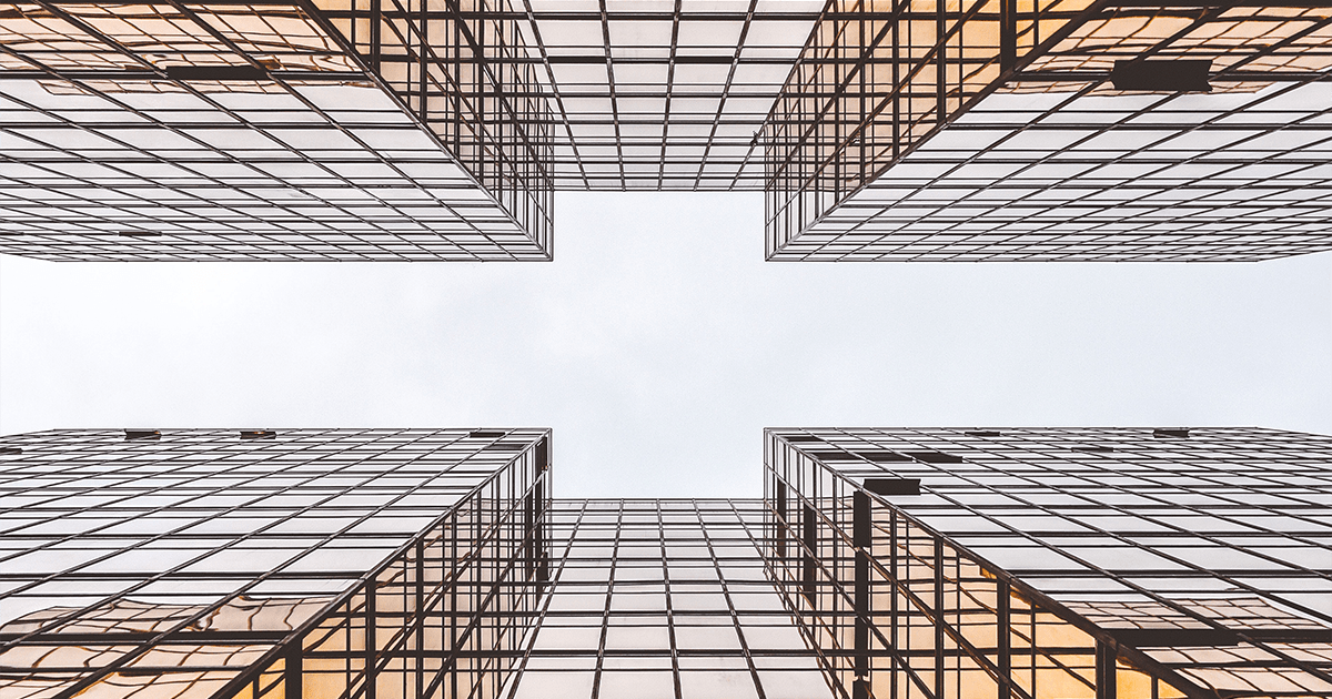 Low-angle view looking straight up between four modern glass grid skyscrapers against a bright white sky.