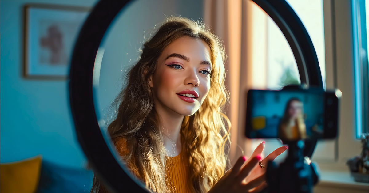Young woman filming herself with a smartphone through a ring light.