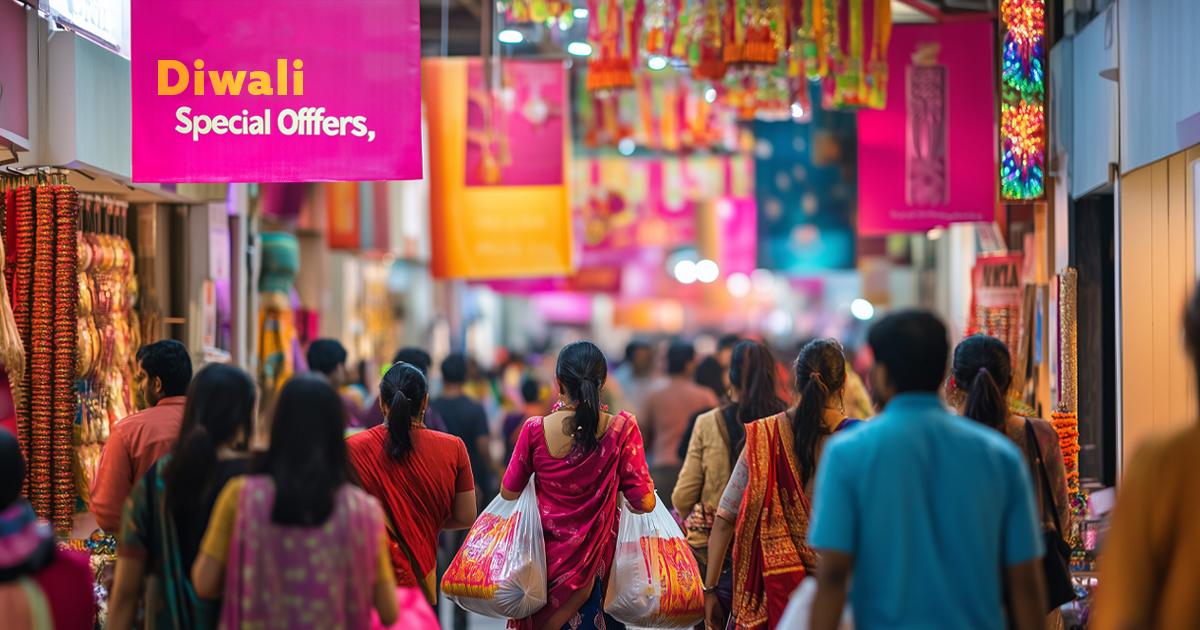 Crowded shopping area in India decorated for Diwali, with shoppers walking beneath colorful banners.