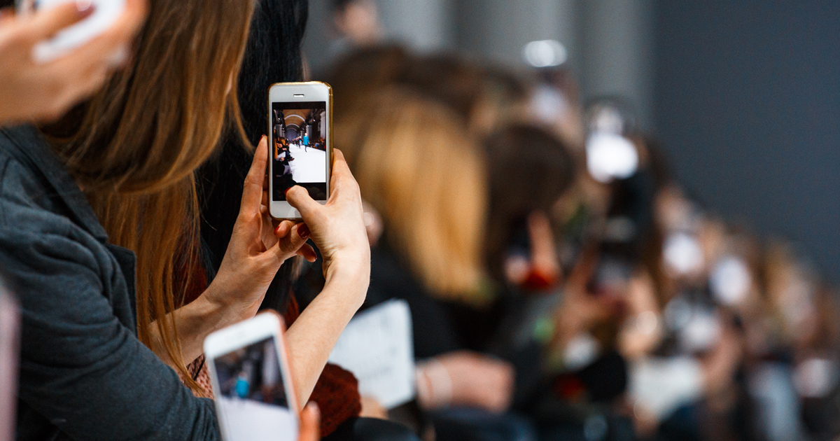 Woman taking photo on smatrphone while watching fashion show from the front row.